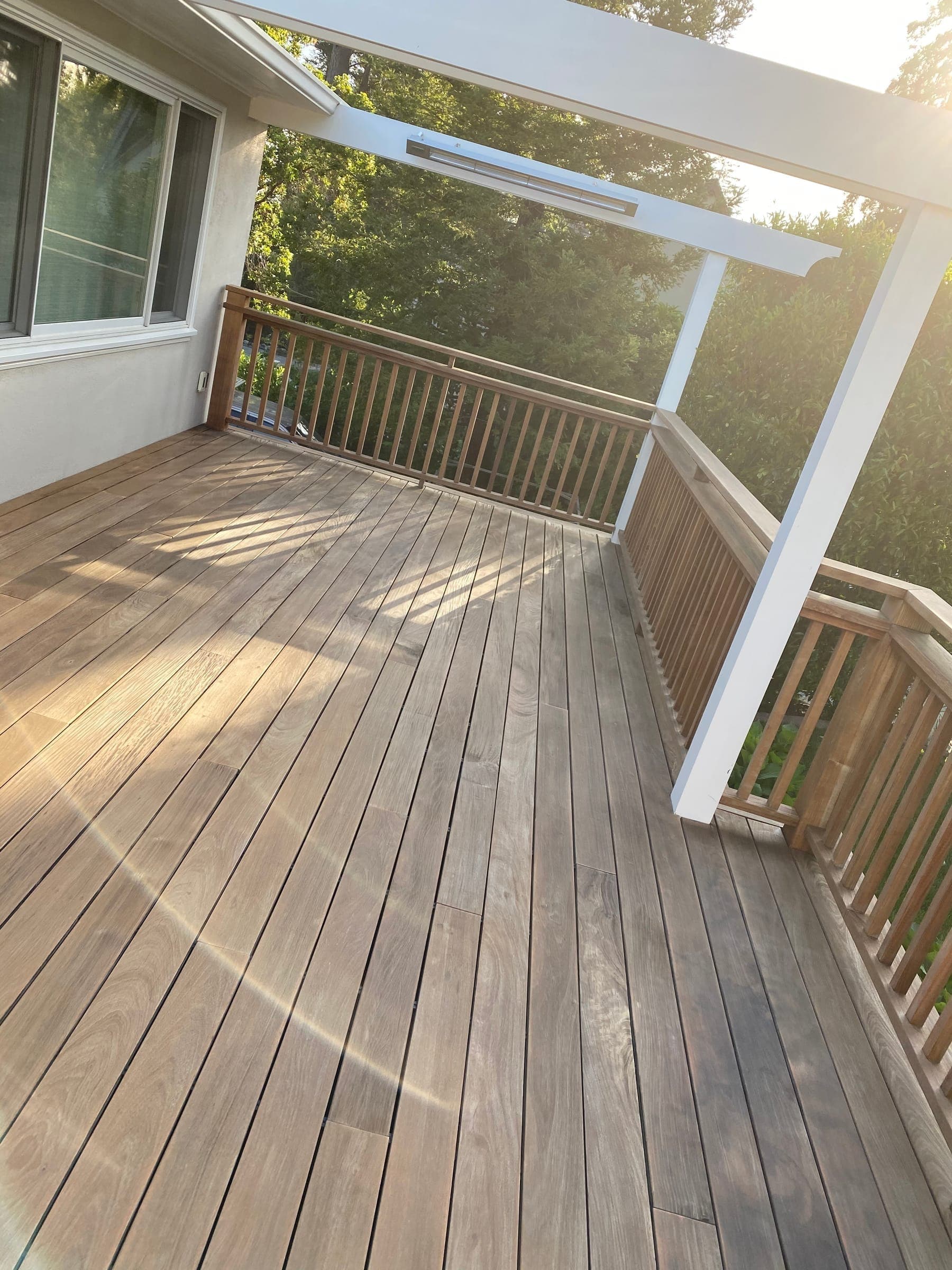 Corner of the new ipe deck with rail posts and white pergola in evening light