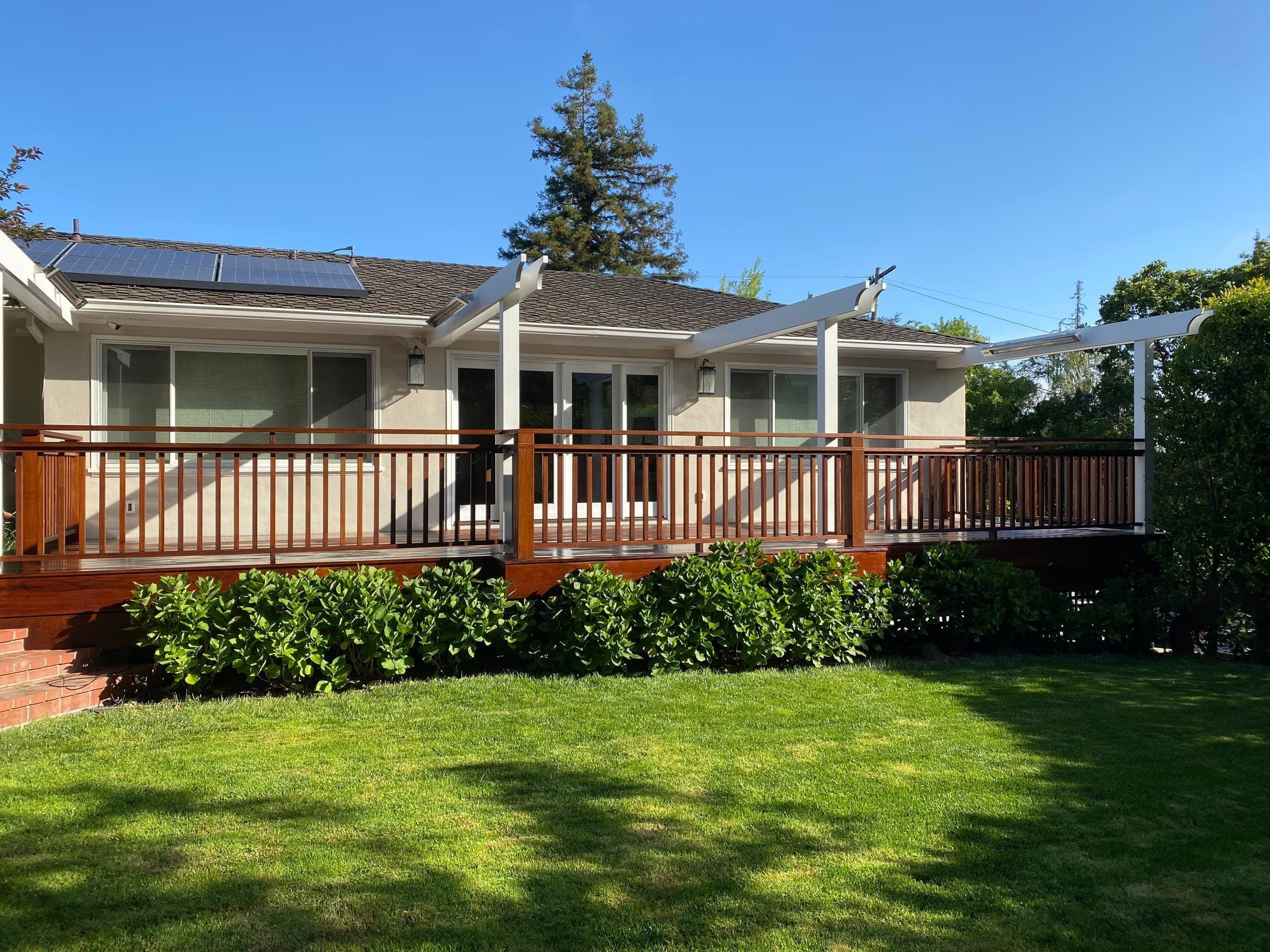 Completed elevated ipe deck with wood railing and white pergola across the back of the house